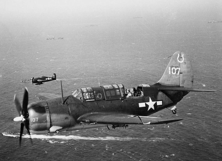 A U.S. Navy Curtiss SB2C-3 Helldiver of Bombing Squadron VB-7 in flight over ships of Task Force 38 after completing an attack against Japanese shipping 40 km north of Quinchon, French Indochina, in January 1945.