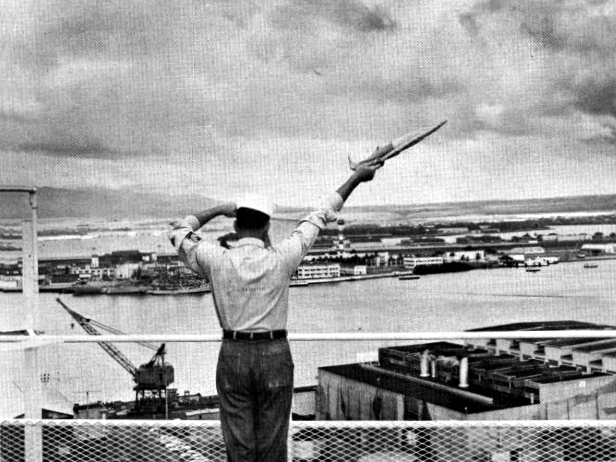 A U.S. Navy signalman, sends a semaphore message to a ship from the top of the Pearl Harbor Control Tower.