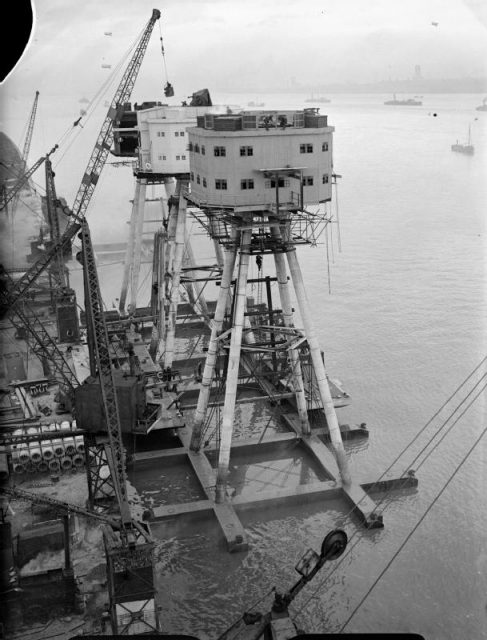 120 foot Maunsell anti-aircraft forts for use in the Mersey Estuary under construction at Bromborough Dock. Here they are well on the way to completion with the accommodation block fitted to the four long legs that will rest on the sea bed.