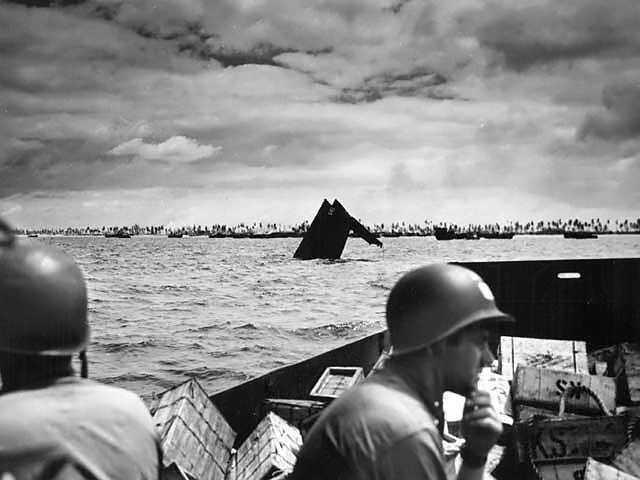 U.S. Coast Guardsmen ferrying supplies pass an LCM-3 which has taken a direct hit at Tarawa.