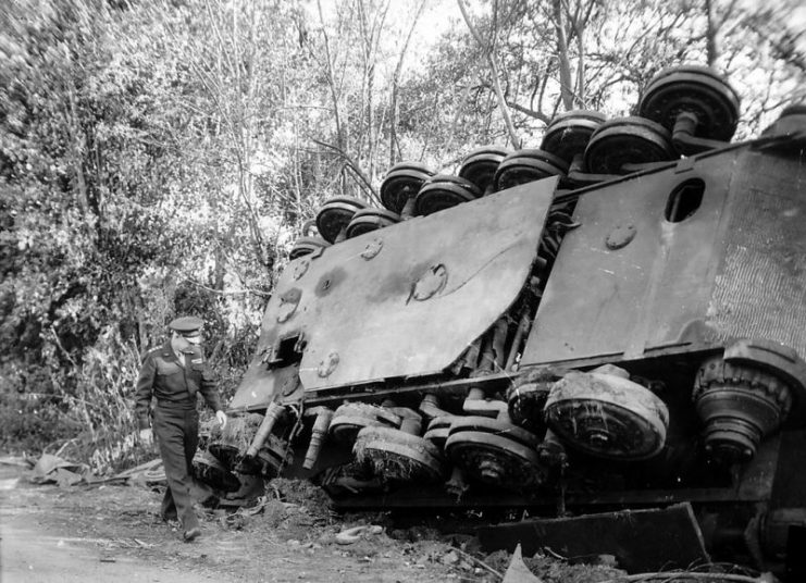 SHAEF commander Gen. Eisenhower walks by an overturned Tiger II. The overlapping, non-interleaved steel-rim roadwheel arrangement is visible.