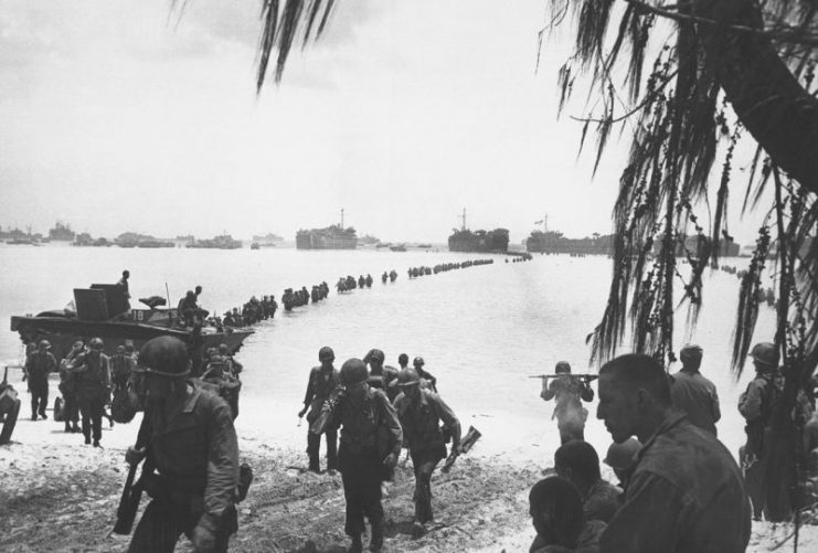 Army reinforcements disembarking from LST’s form a graceful curve as they proceed across coral reef toward the beach, Saipan.