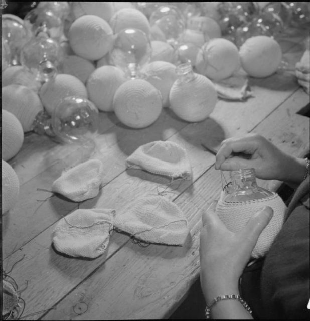 A close-up view showing knitted woollen jackets being fitted the glass flasks of sticky bombs at a factory workshop, somewhere in Britain. The jackets are fastened by means of a drawstring around the neck of the flask. The woollen jackets will soon be coated with adhesive to enable them to stick to their target before detonation.