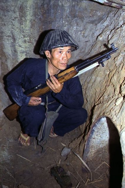 A Viet Cong soldier crouches in a tunnel with an SKS rifle.