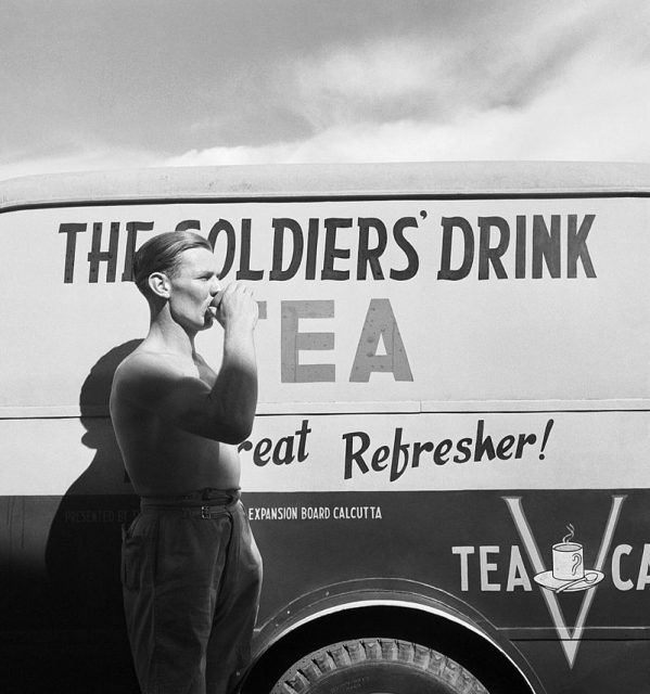 India 1944: A soldier drinking a cup of tea next to a Red Cross Mobile tea wagon at Calcutta airport.