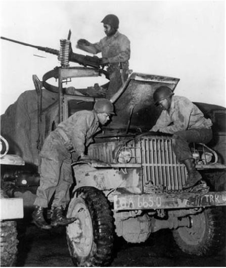 Members of the Red Ball Express repair a 2-1/2 ton truck, while a crewman at a machine gun keeps watch.