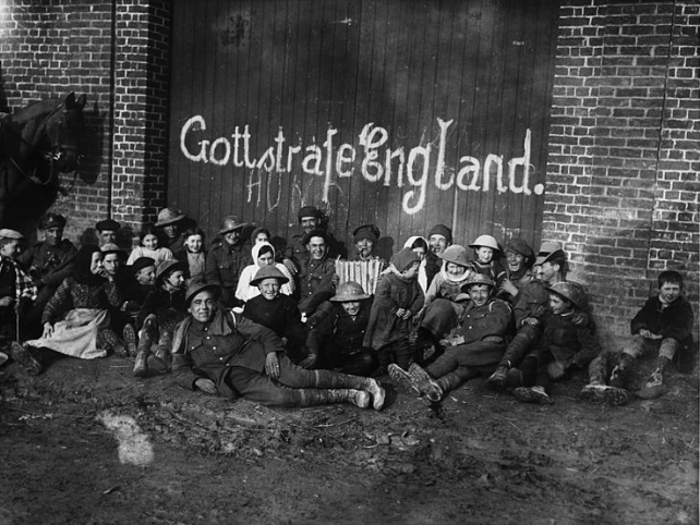 Soldiers and locals outside a German grafittied building, during World War I. The door of the building is daubed with “Gott strafe England”
