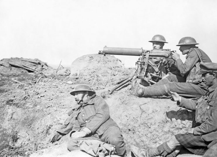 Four men in a barren landscape with a tripod-mounted machine gun