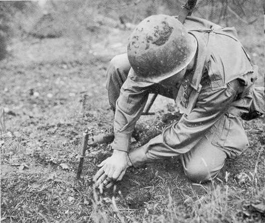 An American infantryman probes for mines using a knife.