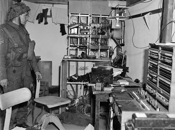 Corporal W. Nichorster of the Royal Canadian Corps of Signals examines the telephone switchboard in the underground bunker of a German radar station at Beny-sur-Mer. Although the site was originally intended to be taken on D-Day, a series of problems delayed its capture until 11 June.