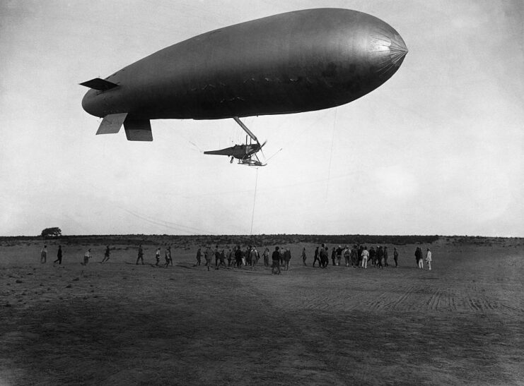 People standing below a blimp hovering over the ground