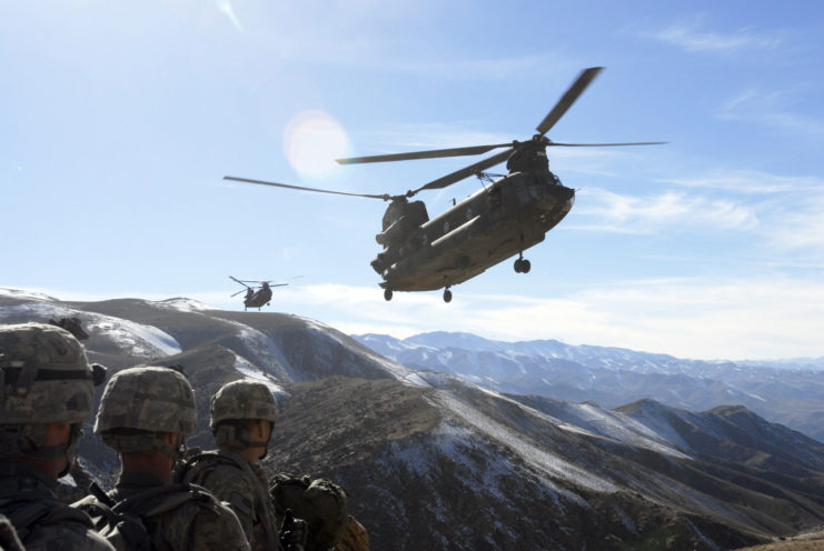 Two Boeing CH-47 Chinooks flying over a group of soldiers