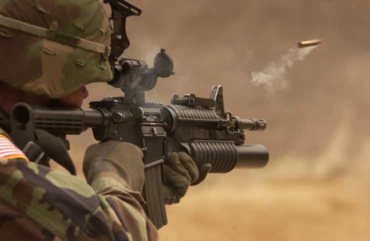 A shell casing flies out with a trail of smoke as U.S. Army Pfc. Michael Freise fires an M-4 rifle.