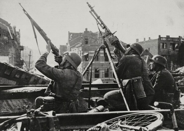 Two German soldiers aiming their rifles to the sky while another sits beside them