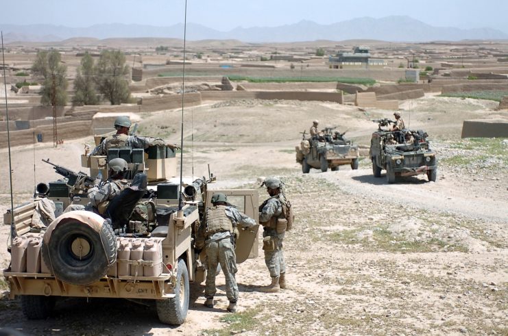 Two military vehicles driving past one that/s parked along the side of a dirt road