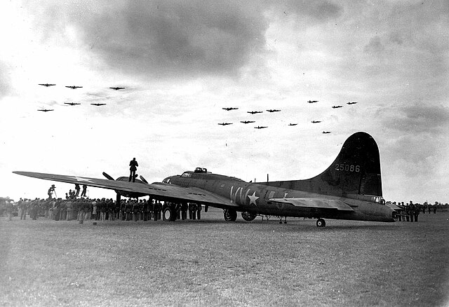 Boeing B-17 Flying Fortresses flying over another parked on the grass
