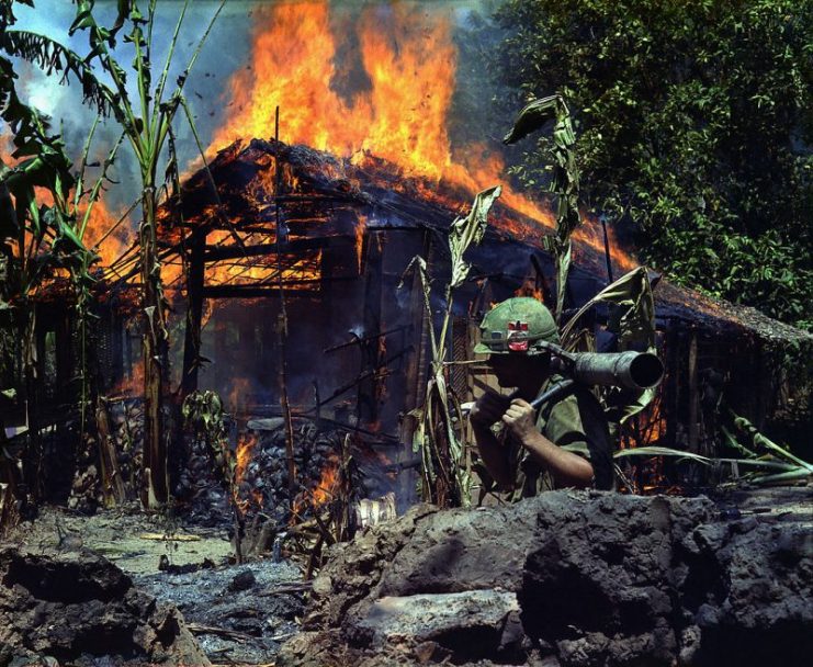 Mỹ Tho, Vietnam. A Viet Cong base camp being burned down. In the foreground is Private First Class Raymond Rumpa, St Paul, Minnesota, C Company, 3rd Battalion, 47th Infantry, 9th Infantry Division, with 45 pound 90 mm recoilless rifle. April 1968
