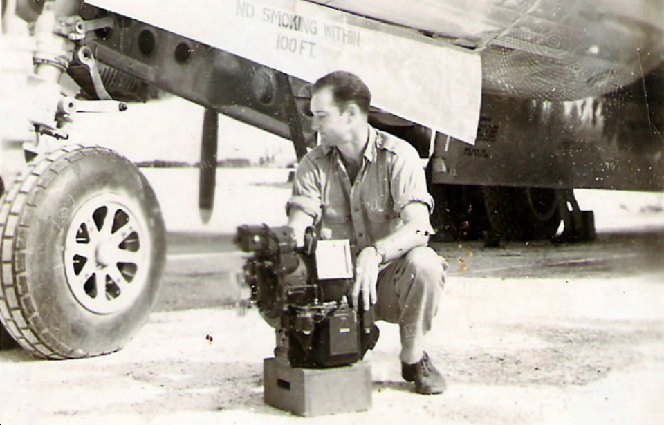 Thomas Ferebee crouching beside a Norden bombsight outside of the Boeing B-29 Superfortress 'Enola Gay'