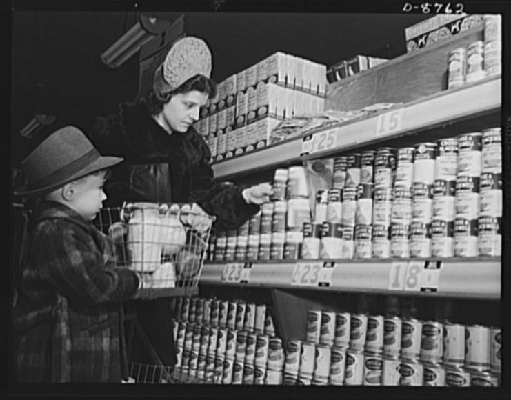 Preparation for point rationing. A shopper and her son carefully weigh posted price and point values in purchasing canned foods under war ration book two