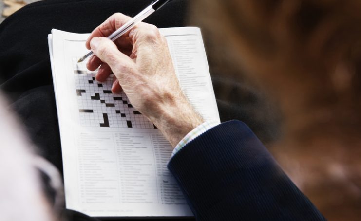 Close up of senior man’s hand with pen on crossword puzzle