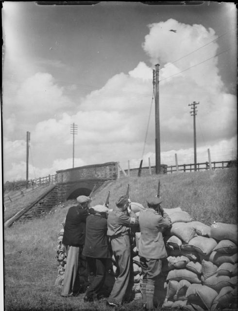 Local Defence Volunteers (LDV) aim their rifles at a passing RAF aircraft from behind a sandbagged position, 30 July 1940.