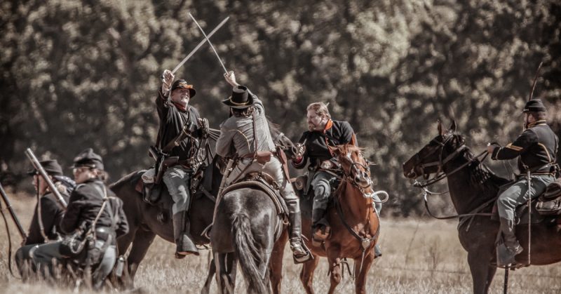 Union and Confederate cavalry troops sword fight and engage in combat during a Civil War reenactment.
