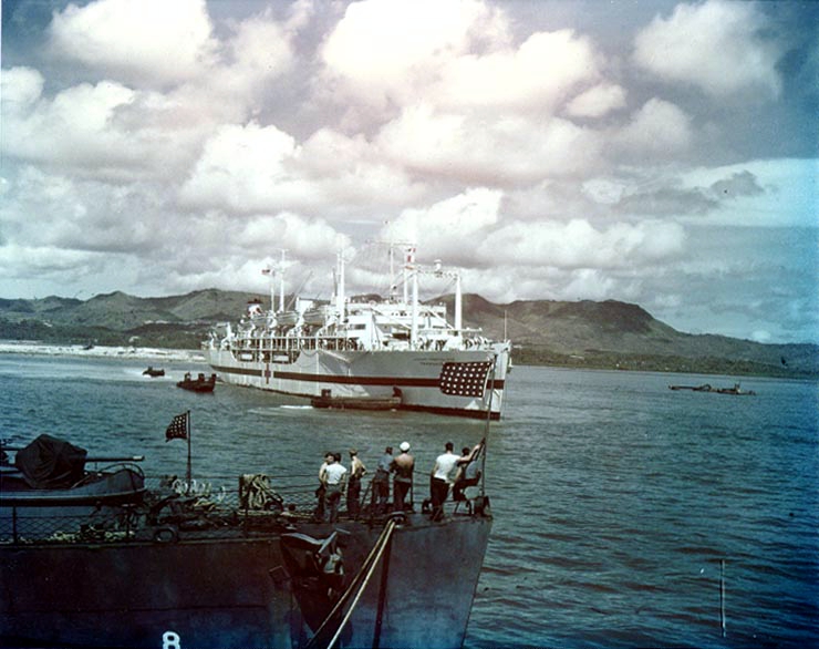 The U.S. Navy hospital ship USS Tranquillity (AH-14) arrives at Guam, carrying survivors of the heavy cruiser USS Indianapolis (CA-35), 8 August 1945. The bow of the destroyer escort USS Steele (DE-8) is visible in the foreground.