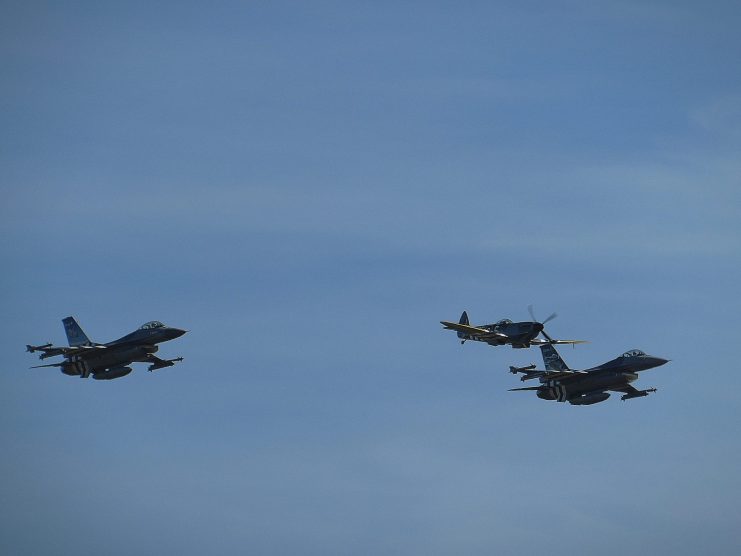 Spitfire flanked by two Belgian F16 fighting falcons featuring “invasion markings”.