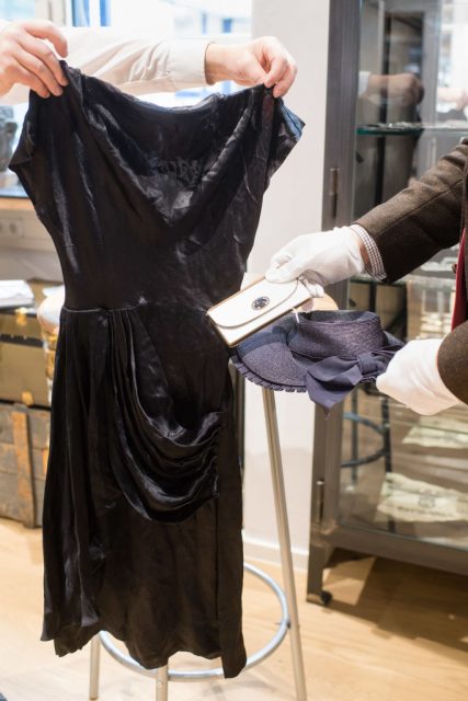 Two men hold a black silk cocktail dress, a hat and a wallet from Adolf Hitler’s partner Eva Braun. GETTY