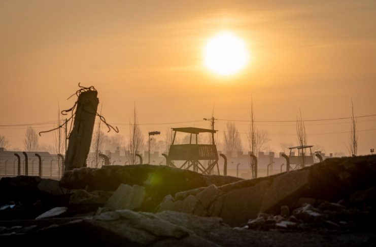 The sun rises early in the morning behind the ruins of a gas chamber, the barbed wire fences and watchtowers of the former Auschwitz-Birkenau extermination camp. Photo: Kay Nietfeld/dpa (Photo by Kay Nietfeld/picture alliance via Getty Images)
