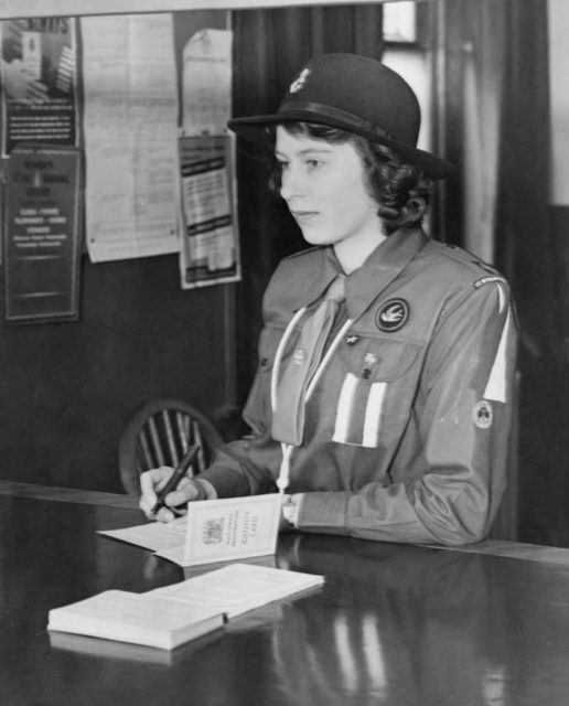 Queen Elizabeth II signing a card while sitting at a table