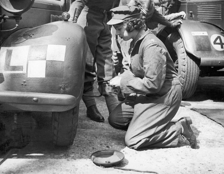 Queen Elizabeth II kneeling along the side of a car