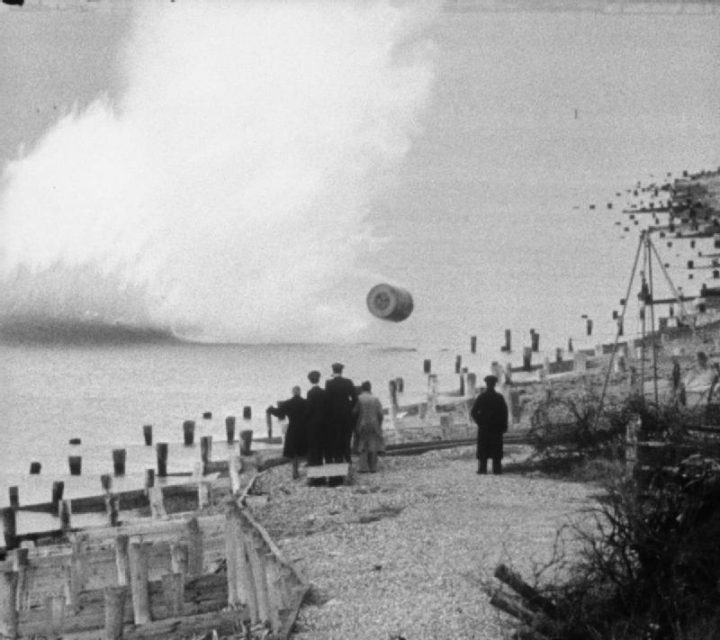 Barnes Wallis and others watch a practice Upkeep bomb strike the shoreline at Reculver, Kent.