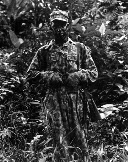 An Alamo Scout poses for a photo in full mission attire. He is wearing the M1942 Jungle Suit and is armed with an M1 Carbine. His fatigue cap has been hand-painted to match his Jungle Suit. New Guinea, January 1944.