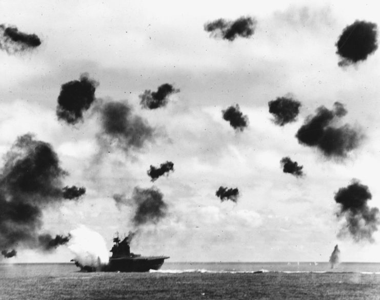 USS Yorktown (CV-5) is hit on the port side, amidships, by a Japanese Type 91 aerial torpedo during the mid-afternoon attack by planes from the carrier Hiryu, in the Battle of Midway, on 4 June, 1942. Yorktown is heeling to port and is seen at a different aspect than in other views taken by USS Pensacola (CA-24), indicating that this is the second of the two torpedo hits she received. Note very heavy anti-aircraft fire.