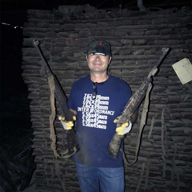 Welgand with two Carbines. Behind him can be seen stacks of more rifles.