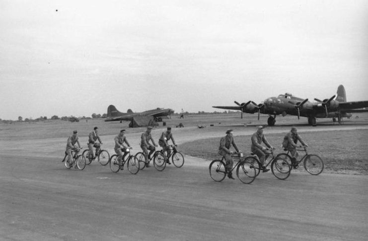 92d Bomb Group riding bikes past B-17 Flying Fortresses B-17F (PY-T, serial number 42-3165) and B-17F (UX-H, serial number 42-5745) nicknamed The Fuhrer the Better, at Alconbury.