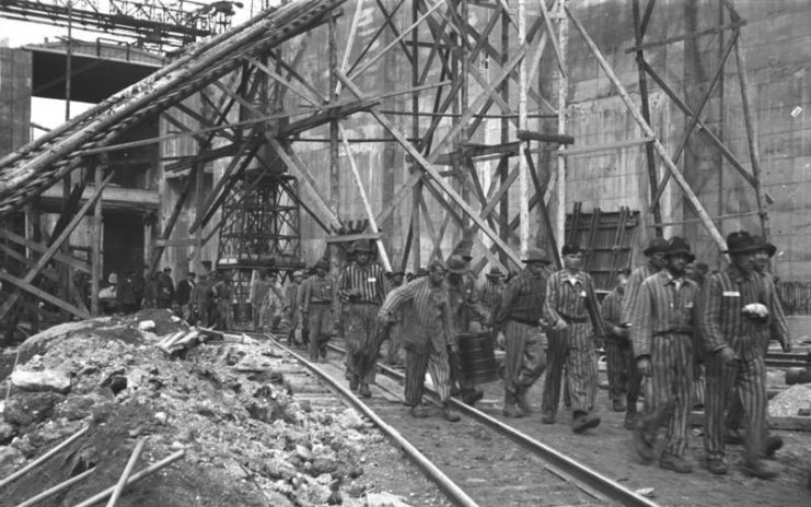 A column of forced laborers walking next to wooden scaffolding of the Bremen U-boat pens. Bundesarchiv CC BY-SA 3.0