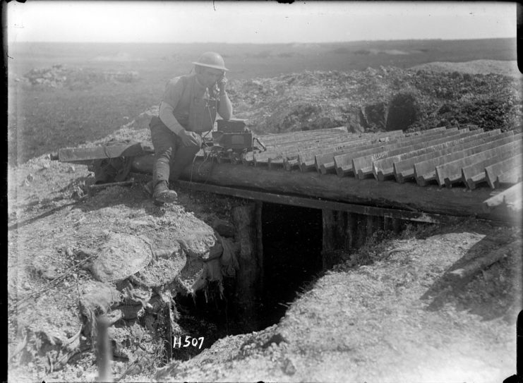 A New Zealand signaller sitting on the roof of his dugout using a field telephone.