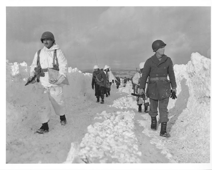 American infantrymen of an armored division march up a road southeast of Born, Belgium. Note the height of the snow bank on either side of the road. January 22 1945