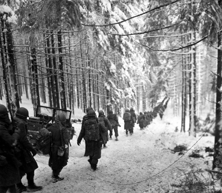 American soldiers of the 289th Infantry Regiment march along the snow-covered road on their way to cut off the Saint Vith-Houffalize road in Belgium on 24 January 1945.