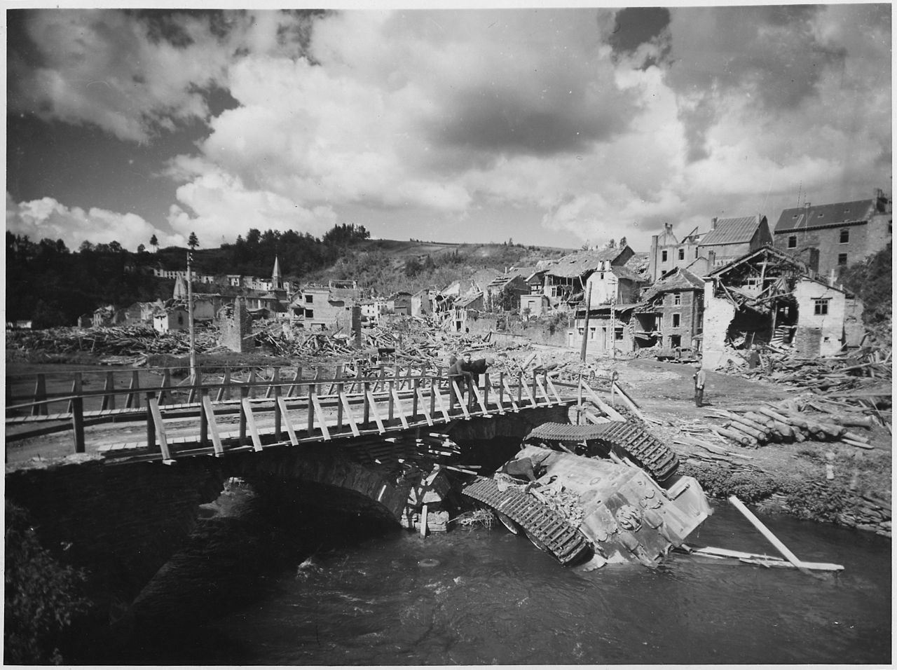 An overturned German Panther lies in a shallow stream alongside a rebuilt bridge in war-ravaged Houffalizo, Belgium.