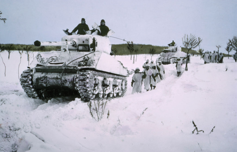 Tank and soldiers moving through the snow during the Battle of the Bulge