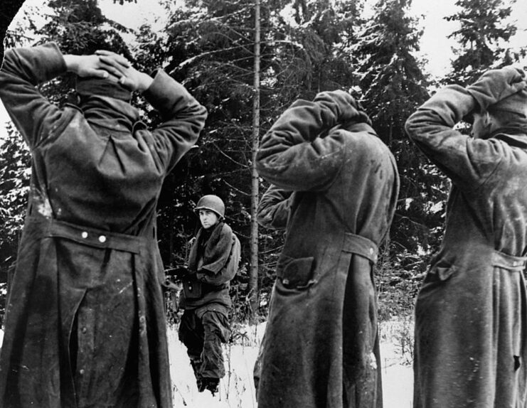 American soldier aiming his weapon at three German prisoners of war (POWs)