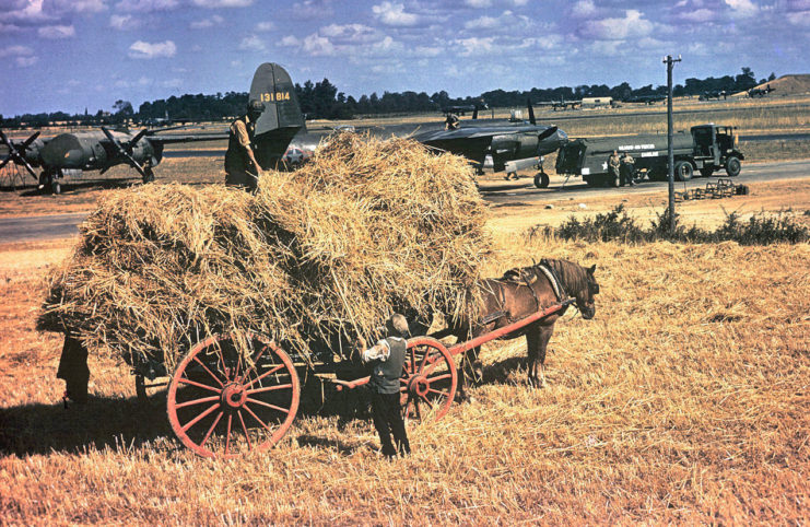 Farmers collect hay at Andrews Field whilst personnel of the 322nd Bomb Group work on a B-26 Marauder (serial number 41-31814) nicknamed Bag Of Bolts.
