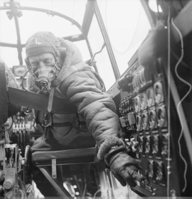 Flying Officer J B Burnside, the flight engineer on board an Avro Lancaster B Mark III checks settings on the control panel from his seat in the cockpit.