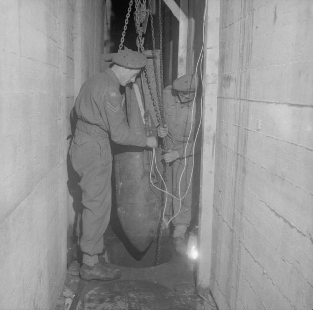 In preparation for the demolition of the U-Boat pens at Hamburg, sappers of 224 Field Company, Royal Engineers, lower a German 250 kilo bomb into a well hole in the floor of the pens.