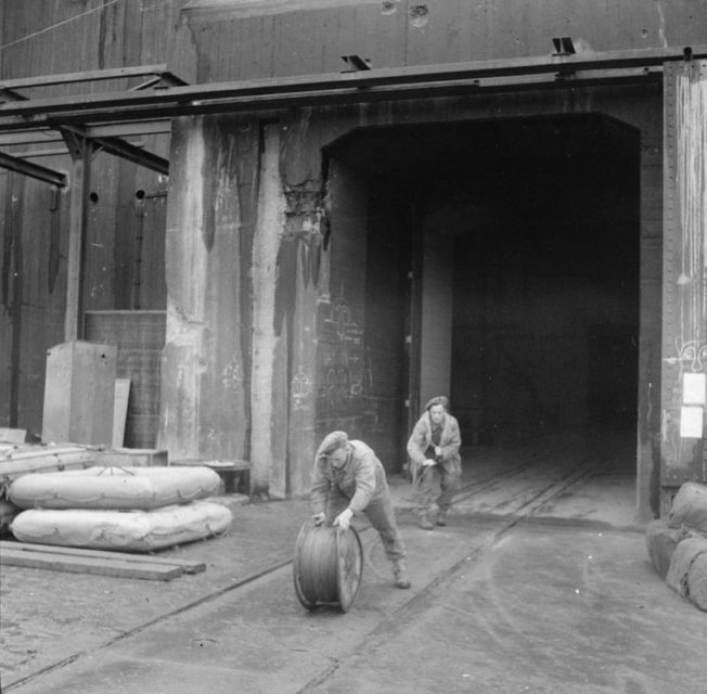 In preparation for the demolition of the U-Boat pens at Hamburg sappers of 224 Field Company, Royal Engineers, roll out the firing cable once all the explosive charges are in place.