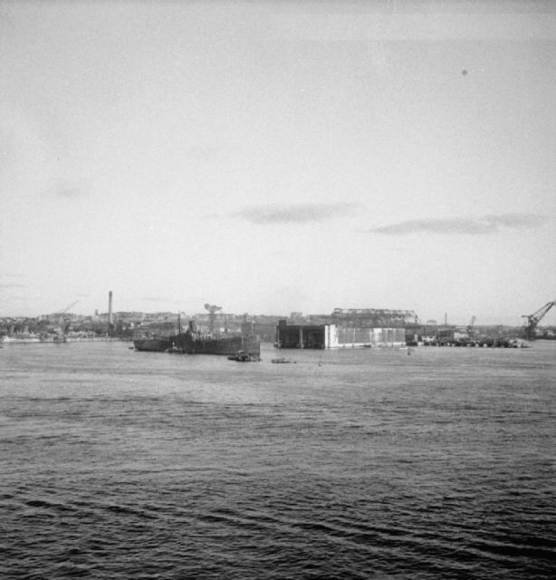 In preparation to demolish the U-Boat pens at Kiel an old cargo-ship is moored across the entrance to the pens to stop the blast damaging private property across the river.