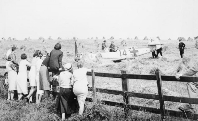 Locals watch as troops and police inspect Messerschmitt Bf 109E-1 (W.Nr. 3367) “Red 14” of 2./JG52, which crash-landed in a wheatfield at Mays Farm, Selmeston, near Lewes in Sussex, 12 August 1940. Its pilot, Unteroffizier Leo Zaunbrecher, was captured.